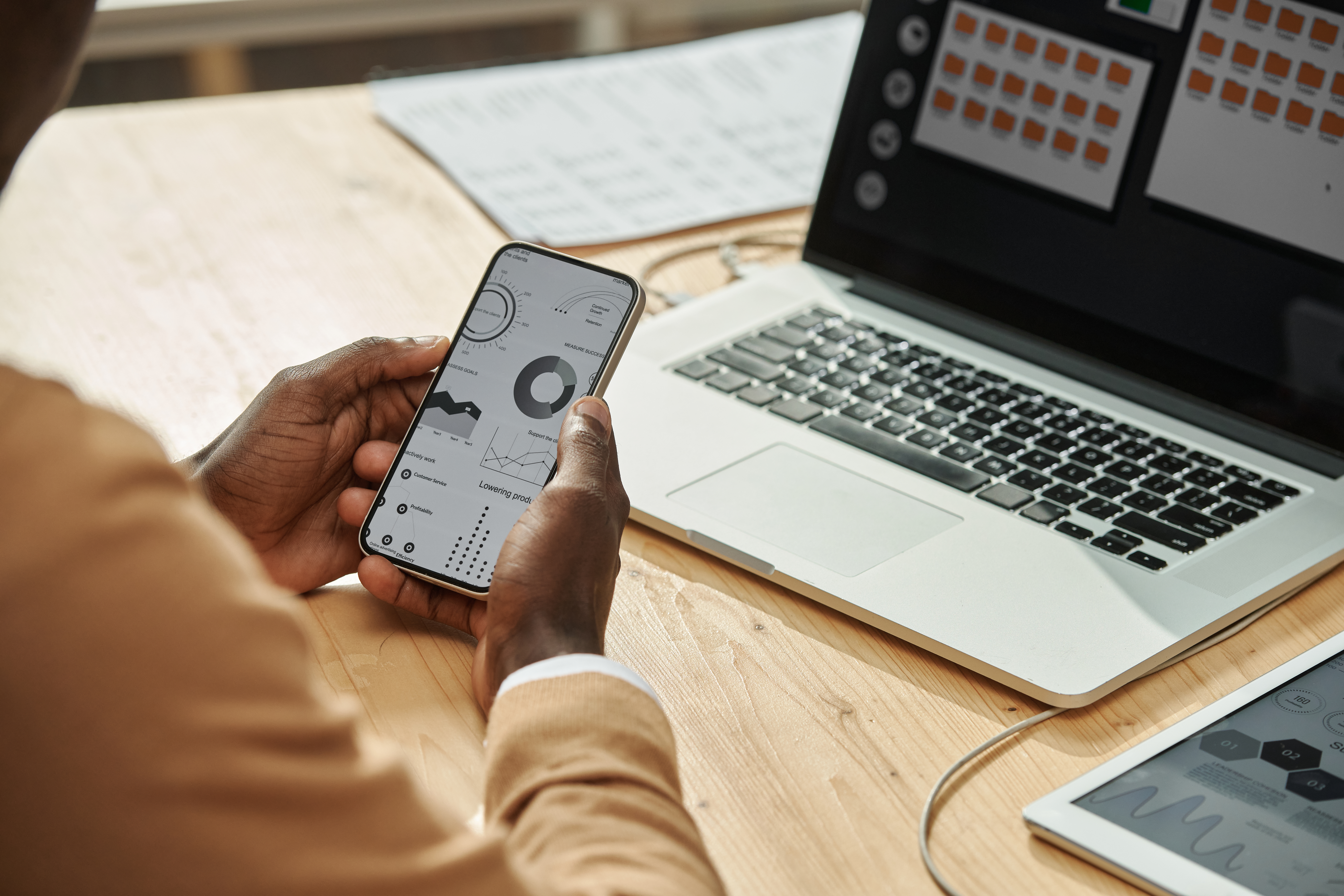 Close-up of businessman examining financial graphs on his smartphone while working on laptop at table