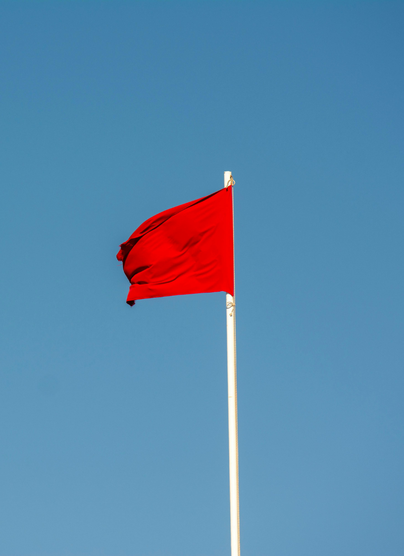 a solid red flag on a white pole waving in the wind on the background of a blue sky